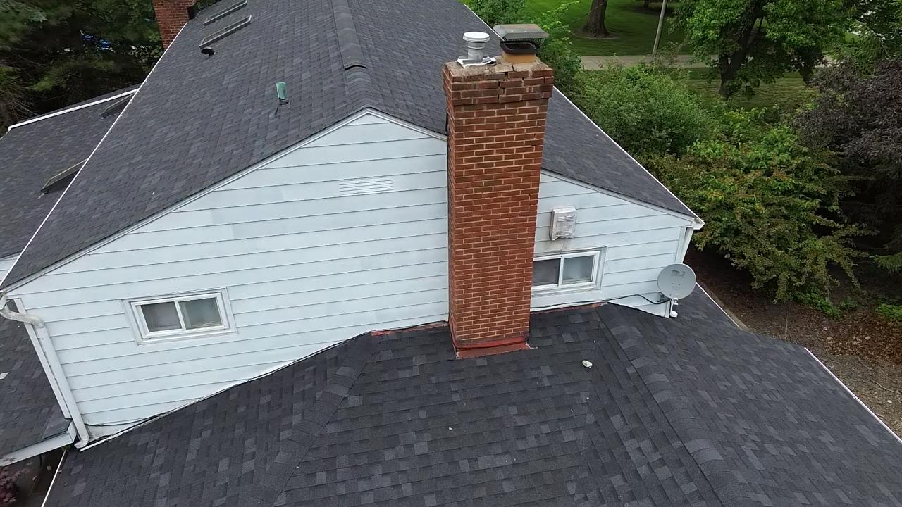 Why Is My Chimney Leaking When It Rains? The 5 Usual Causes in Cleveland Homes 3 Drone view of a brick chimney where it meets an asphalt shingle roof, showing the flashing at the roofline