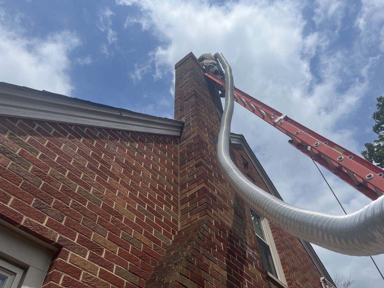 Gas Fireplace Insert vs Gas Logs: Which Is Right for Your Cleveland Home? 2 Technician on a ladder at the top of a brick chimney feeding a flexible metal chimney liner up the outside of the chimney